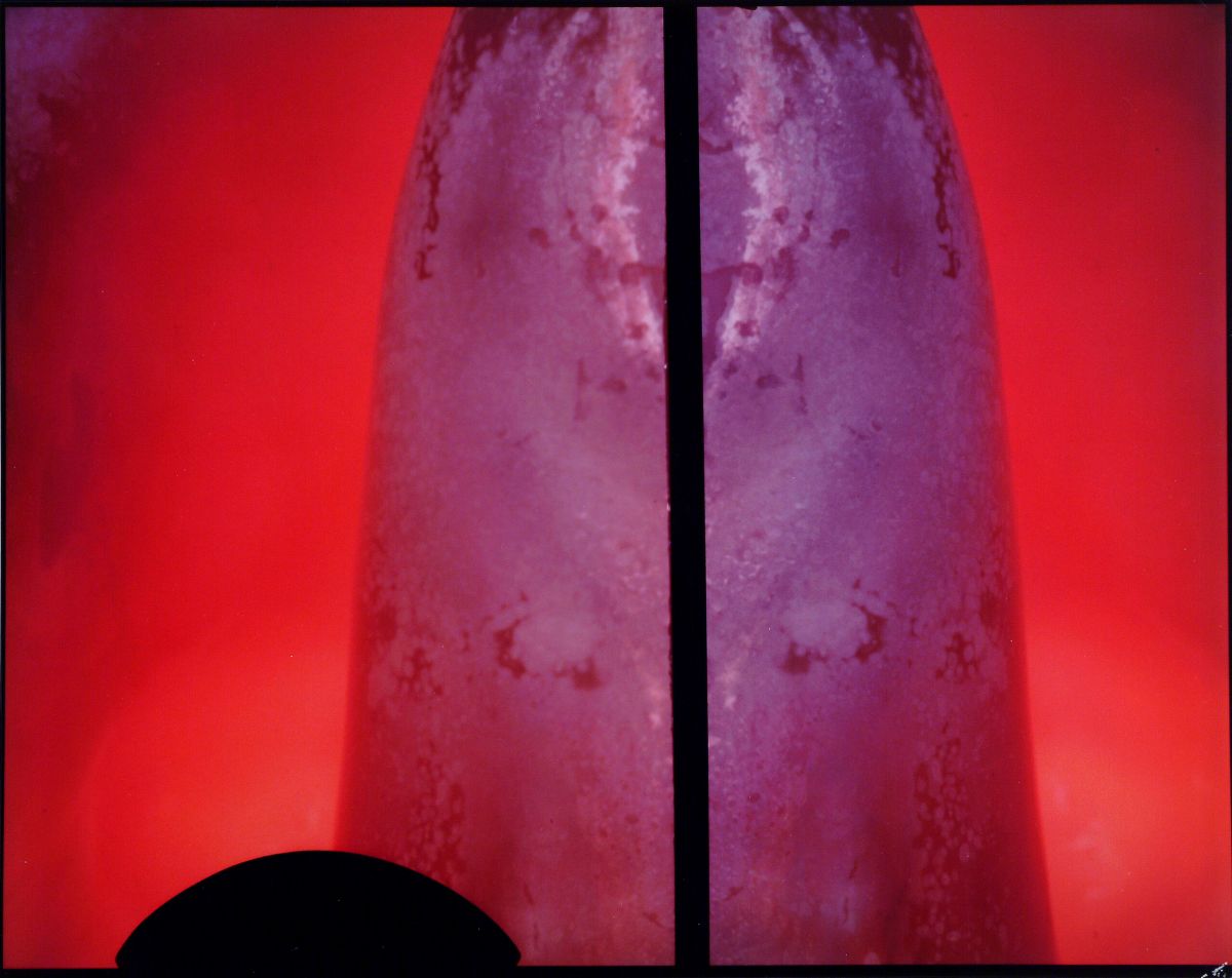The background is red. Against the red, in the middle, a purple shape spans from top to bottom. In the center of the work, a thin black line runs vertically splitting the image in half. On the bottom left, a black oval shadow is visible.