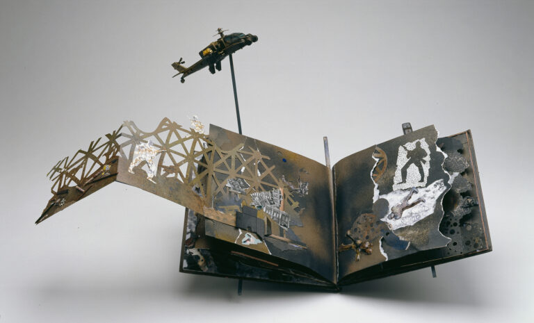 An artist book sits open on a grey background. The open pages reveal a collage filled with scenes of war: soldiers, barbed wire, and ammunition. A toy version of a military helicopter protrudes from the cover of the book.
