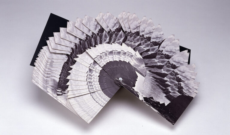 A black and white photo collage, fan-shaped and spread out, showing repeated images of a circular structure and jagged mountain peaks on each section, set against a plain background.