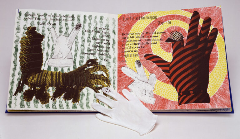 An open art book displays colorful collage illustrations of hands, with text scattered across both pages. A white glove lies in front of the book on a white surface. The background is plain and uncluttered.