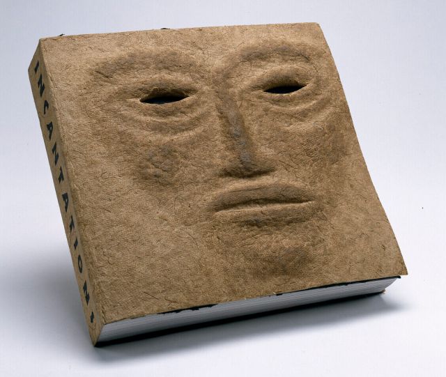A book titled "INCANTATIONS" has a textured cover resembling a human face with hollow eyes and a neutral expression, set against a plain white background.
