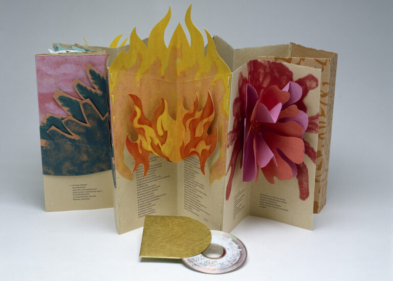 An accordion-style pop-up book made of paper displayed upright and open. The central portion has flames made of paper that extend beyond the top edge of the book. In front of the book there is a CD coming out of its golden holding case.