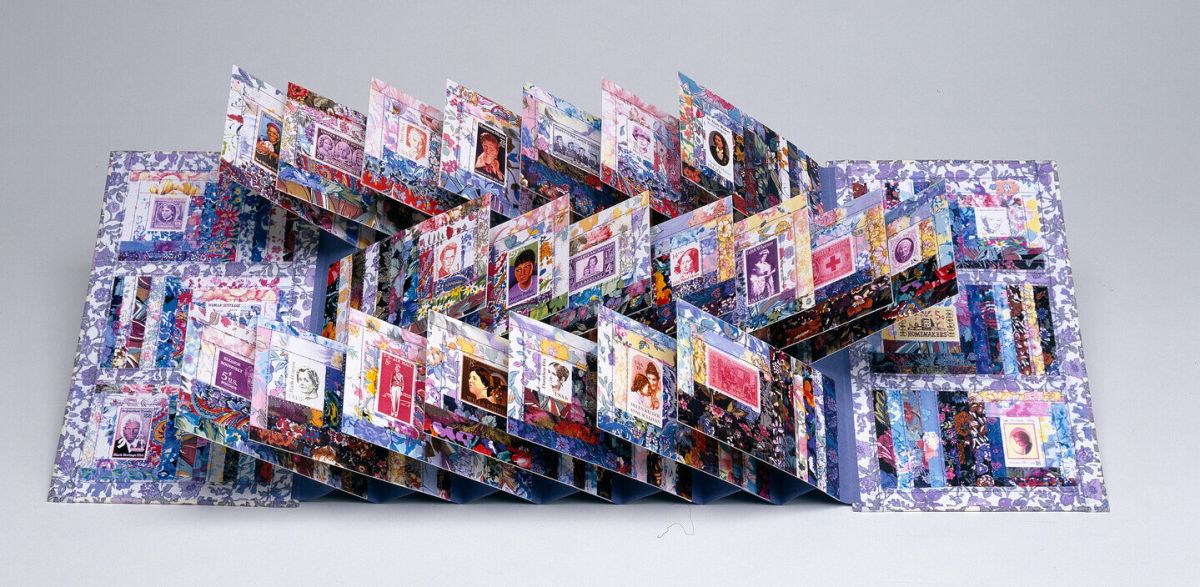 A colorful, intricate pop-up book is open, with multiple panels and pages standing upright, each featuring various images, patterns, and designs on a white background.