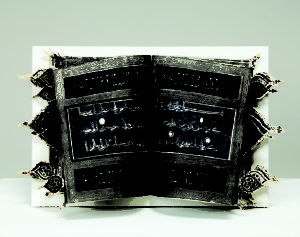 An open book with Arabic text on a dark blue background divided into horizontal sections by decorative silver border. Cut-out arabesques extend out beyond the edge of the book to the right and left.