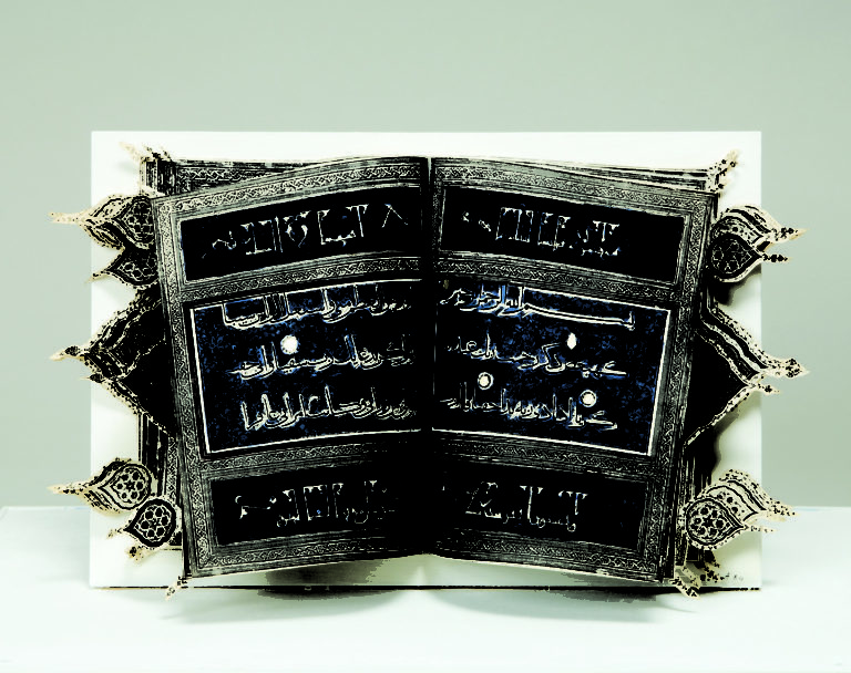 An open book with Arabic text on a dark blue background divided into horizontal sections by decorative silver border. Cut-out arabesques extend out beyond the edge of the book to the right and left.