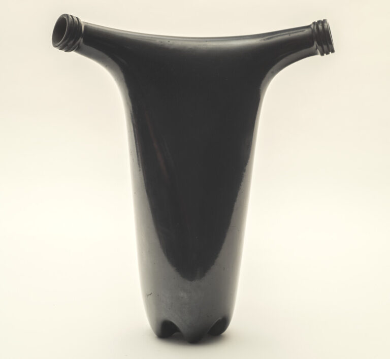 A black sculpture made from two bottles merged together. The shape of the double-spouted vase is reminiscent of a uterus. The shiny black finish gives it a precious look, while the plastic bottle shape juxtaposes this notion of a precious object.