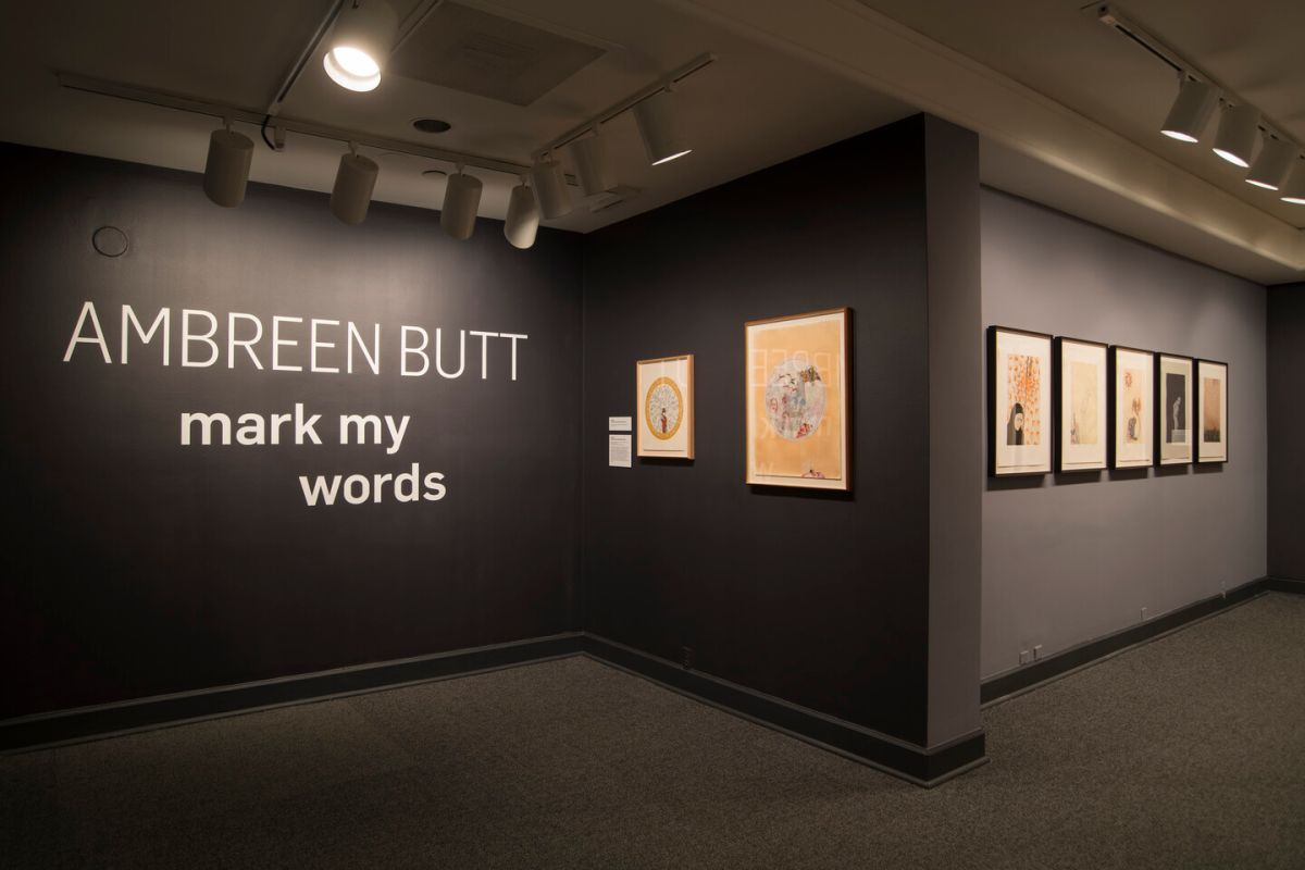 Museum gallery that shows seven prints against dark gray walls and intro text that reads "Ambreen Butt: Mark My Words."