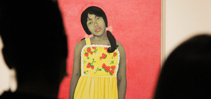Vibrant painting of a young lady with medium skin tone staring out against a bright pink background. The painting is partially obscured by the silhouetted heads of museum visitors.