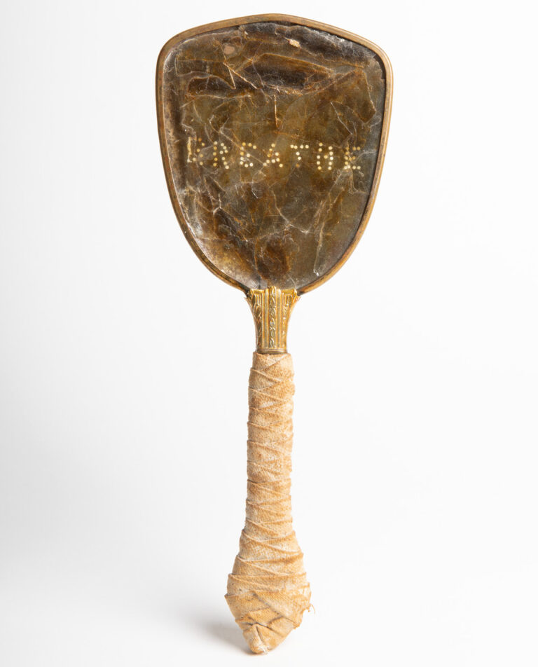 An antique hand mirror against a white background. The handle of the mirror is wrapped in light colored cloth. The head of the mirror is a brown, non-reflective material. The word “breathe” has been perforated onto the surface.