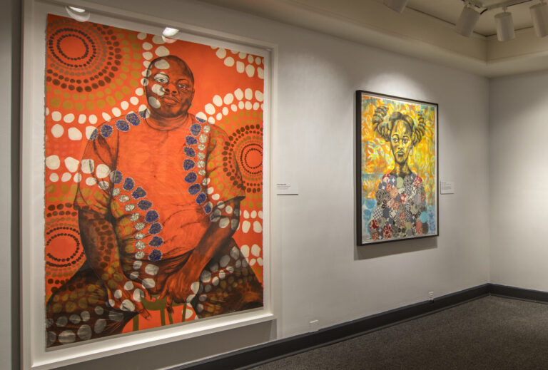 A view of a gallery wall. Three large colorful paintings are hanging on the walls.