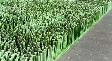 Detail photograph of ceramic sculpture made to look like a patch of lawn. Individual squares consisting of multiple upright blades of porcelain grass, glazed green, fit together to form a lush rectangular field of grass.