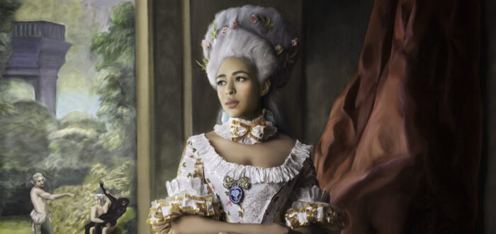 A woman with medium-dark skin tone in historical attire with a large striped gown poses indoors. She wears a powdered wig, and a small white dog sits by her side. A painted background depicts a pastoral scene with a vignette of a violent assault.