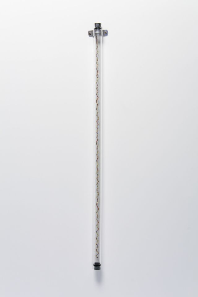 A sculpture of a glass tube affixed to a white wall with a spiraling column of small, multicolored glass beads. The beads are blue, red, yellow, green and black.