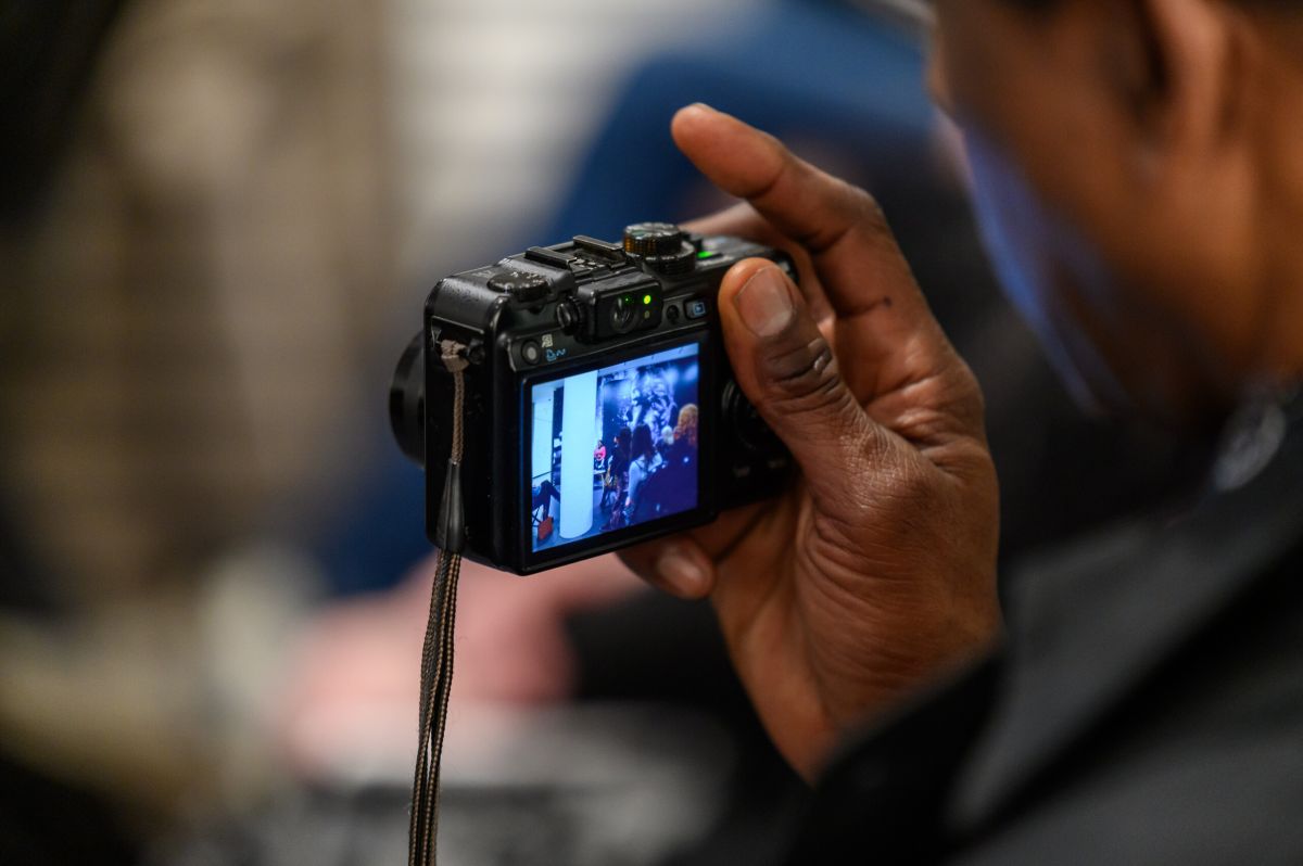 Close-up of a person holding a digital camera, showing a clear image on the screen of people gathered together. The focus is on the camera and the vivid screen display, with the person partially visible.