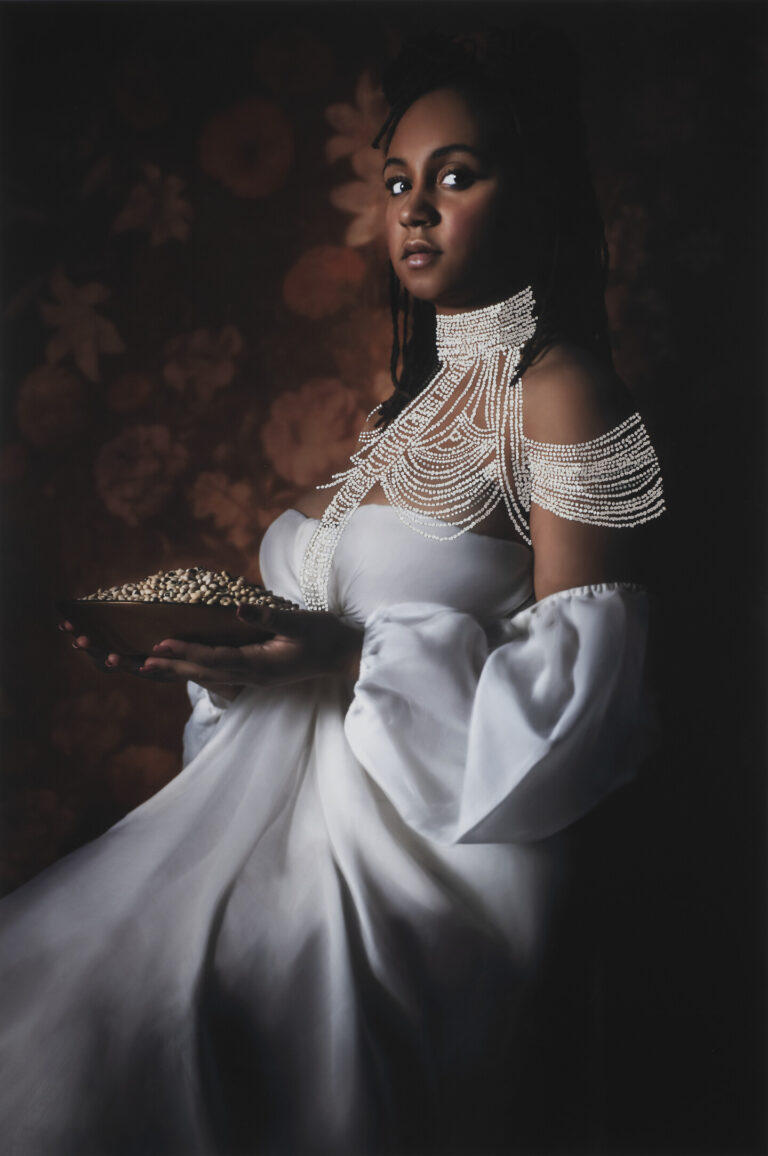 A photograph of a Black woman wearing a long white gown. She is seated and her face is towards the viewer. She holds a plate of black-eyed peas.