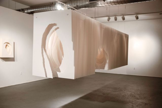 Panels of white paper hung together to look like a long rectangular box suspended from the ceiling a few feet off the ground. Roughly torn holes in the middle of the sheets create a tunnel-like space.