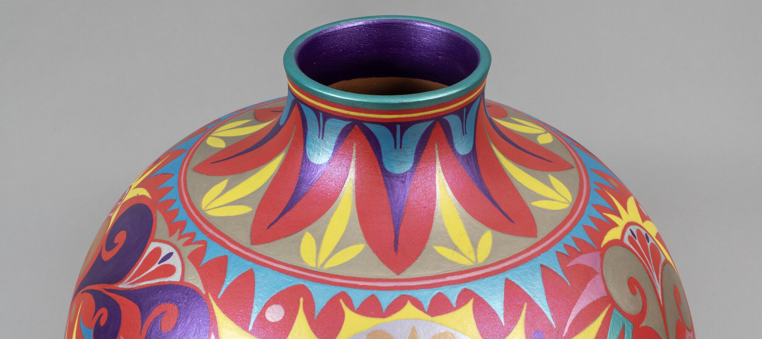 A round ceramic vase with a short neck decorated with intricate geometric and floral patterns painted in red, pink, blue, yellow, and purple.